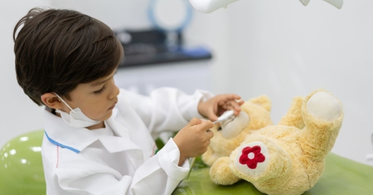 Little kid examining his teddy bear at the dentist office