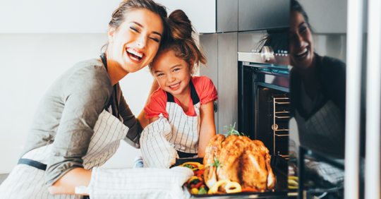 Mom pulling Thanksgiving turkey out of the oven with her little chef