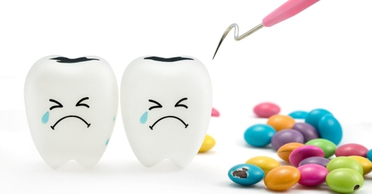 Two cartoon teeth are sad next to candy