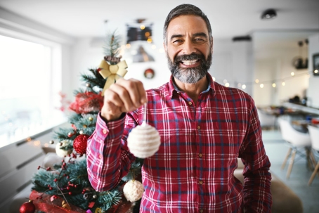 man with christmas ornament standing by tree smiling in plaid shirt