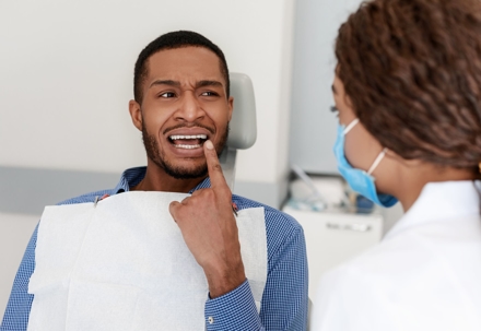 man at the dentist in pain pointing to tooth