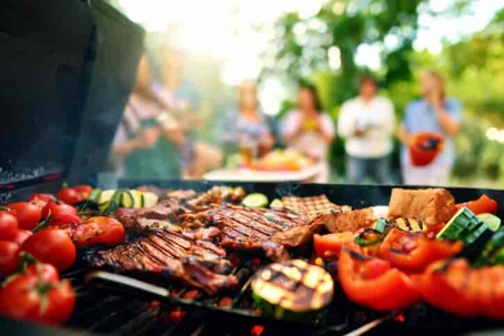 Grilled food on a grill, with people in the background, standing up and blurred from view