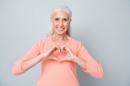 elderly woman holding up heart against grey background