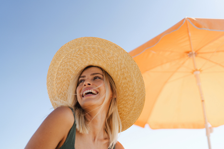 Woman on the beach smiling next to a sunning umbrella