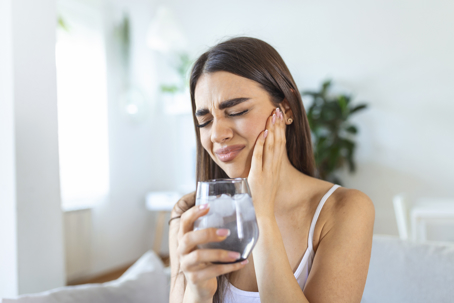 Woman holding cheek in tooth pain while holding an ice water
