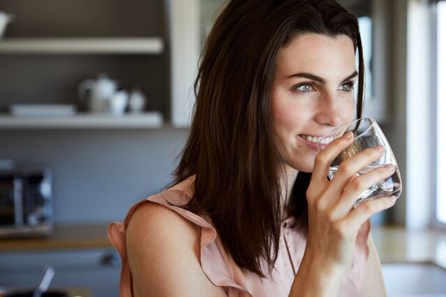 Woman Smiling While Drinking a Glass of Water